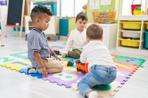 Grupa dzieci bawiących się zabawkami samochodowymi siedzącymi na podłodze w przedszkolu - Zdjęcie, obraz