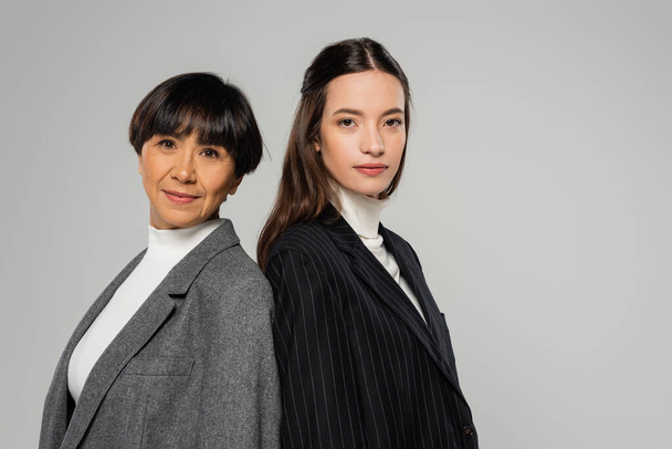 asian mother and daughter in blazers standing back to back and looking at camera isolated on grey - Foto, Bild