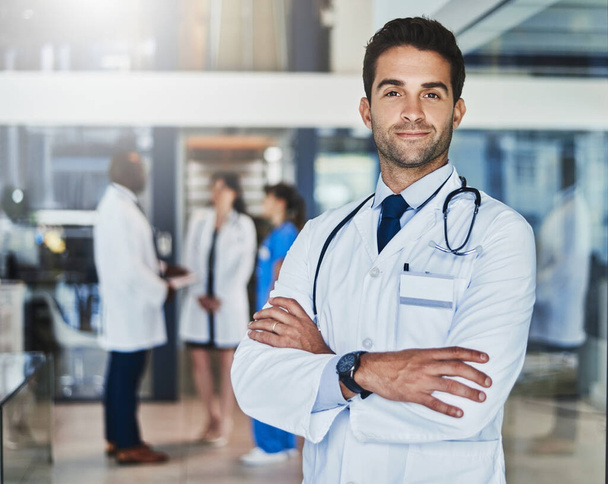 Твое здоровье важнее всего. Портрет уверенного врача, работающего в больнице со своими коллегами на заднем плане - Фото, изображение