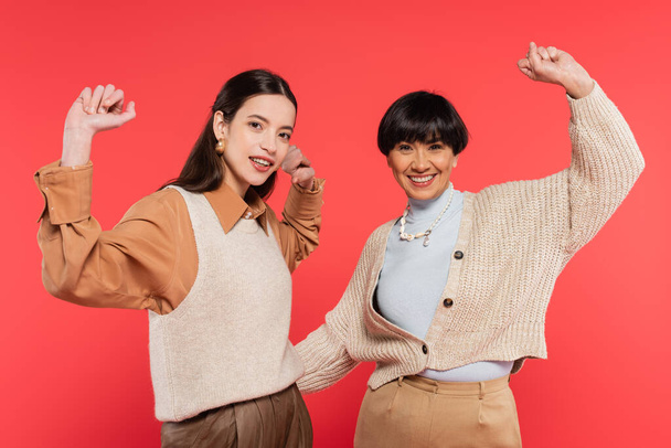 excited asian mother and daughter in trendy clothes showing win gesture isolated on coral - 写真・画像