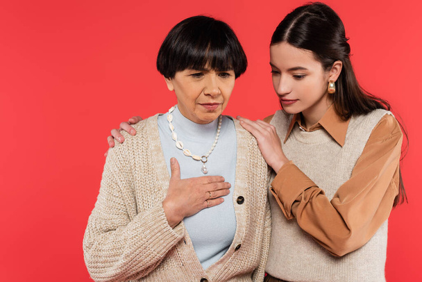 worried asian woman hugging middle aged mother touching chest while feeling unwell isolated on coral  - Fotografie, Obrázek