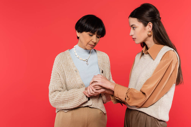 worried asian woman holding hands of upset middle aged mother isolated on coral  - Photo, Image