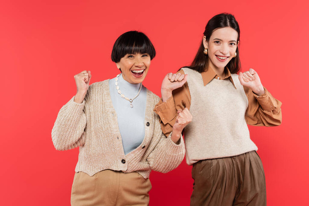 excited asian mother and daughter in stylish clothes celebrating isolated on coral  - Zdjęcie, obraz