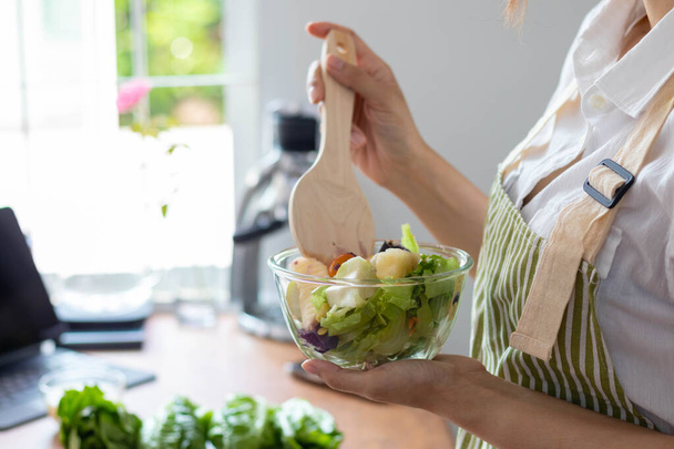若い女性は野菜からサラダを作っています彼女は材料が慎重に選択されているので、清潔で安全なサラダを得るために自宅のキッチンでテーブルの上に用意しています.健康的な食事の準備のアイデア - 写真・画像