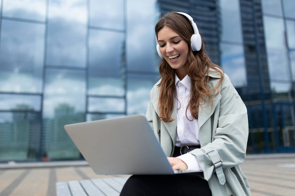 odnoszący sukcesy młody marketer pracujący w słuchawkach na laptopie na zewnątrz. - Zdjęcie, obraz
