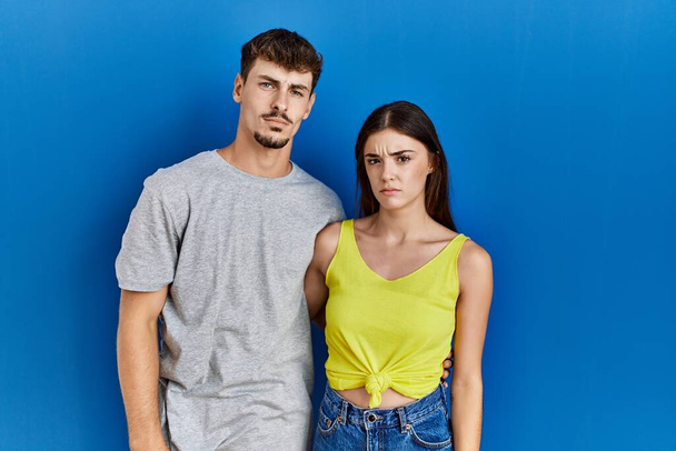 Young hispanic couple standing together over blue background depressed and worry for distress, crying angry and afraid. sad expression.  - Foto, afbeelding