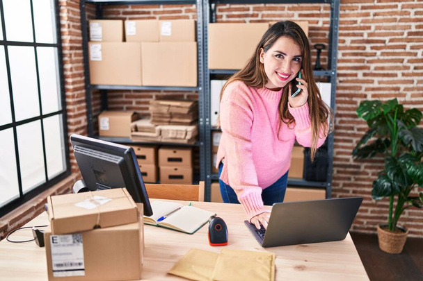 Молода красива іспанська жінка електронної комерції бізнес-працівник, використовуючи ноутбук розмовляє на смартфоні в офісі
 - Фото, зображення