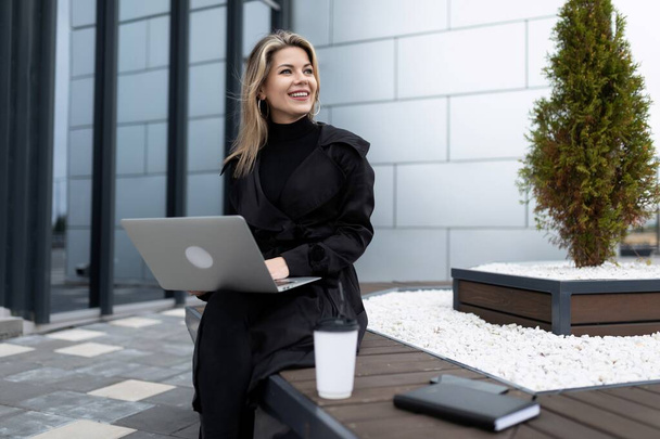 femme d'affaires élégante pendant une pause boire du café dans la rue avec un ordinateur portable dans ses mains. - Photo, image