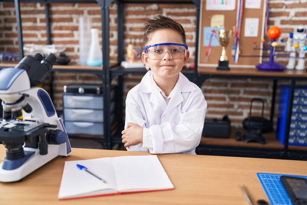Suloinen latino poika opiskelija hymyilee luottavainen seisoo kädet ristissä ele laboratoriossa luokkahuoneessa - Valokuva, kuva