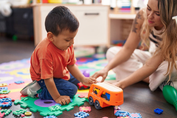 Teacher and toddler playing with cars toy sitting on floor at kindergarten - Foto, imagen