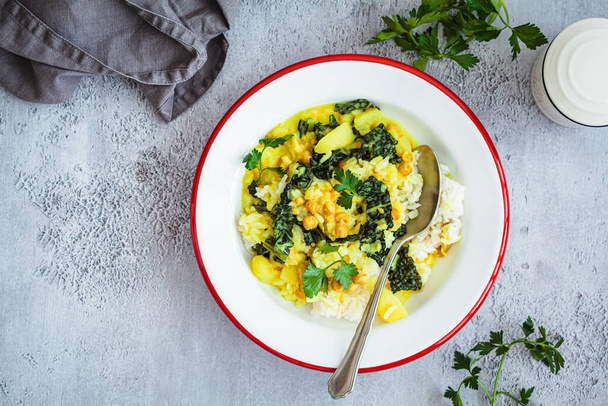 Vegan chickpea potato curry with rice and kale in white plate, gray background, top view. Alternative plant-based eco friendly food concept. - Photo, Image