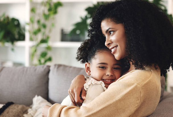 Hug, love and black family by girl and mother on a sofa, happy and relax in their home together. Mom, daughter and embrace on a couch, cheerful and content while sharing a sweet moment of bonding. - Photo, image