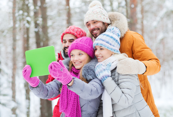 smiling friends with tablet pc in winter forest - Foto, Imagem
