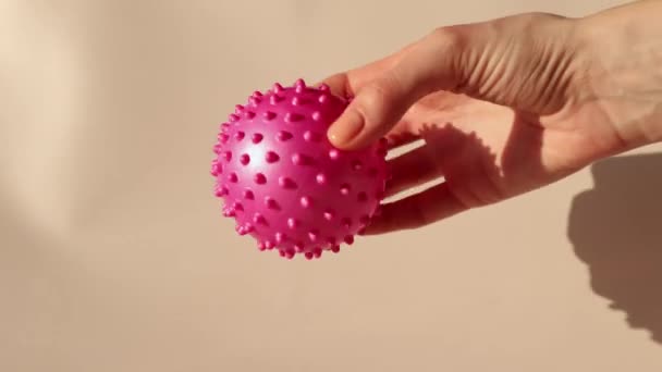 Μια γυναίκα κρατάει μια ροζ μπάλα με καρφιά. Μπάλα μασάζ μπορεί να σας βοηθήσει να απελευθερώσετε πόμολα και πόνο. Οφέλη από τη χρήση ενός μπάλα μασάζ για Myofascial Release. - Πλάνα, βίντεο