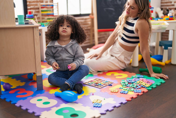 Leraar en peuter spelen met wiskunde puzzelspel zitten op de vloer op de kleuterschool - Foto, afbeelding