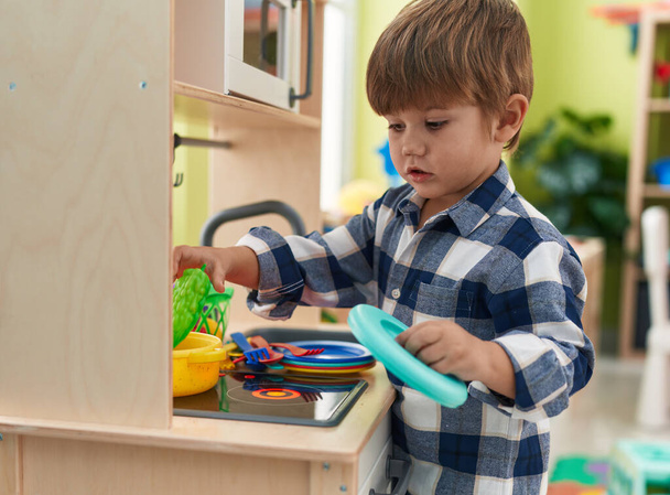Adorable hispanic boy playing with play kitchen standing at kindergarten - Foto, Bild