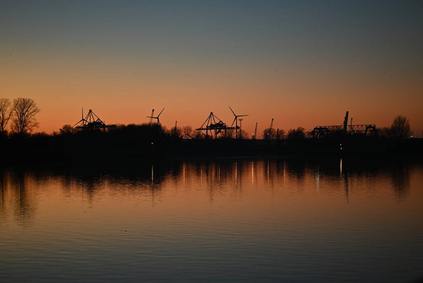 Evening mood besides a river against a container port and a beautyful sunset - Foto, imagen