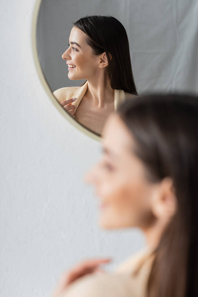 отражение улыбающейся молодой женщины, смотрящей в зеркало ванной  - Фото, изображение