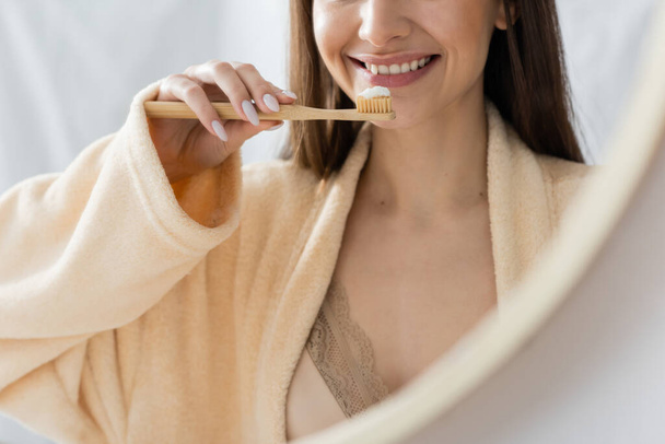 reflection of cropped happy woman with toothbrush brushing teeth in bathroom mirror  - Foto, Bild