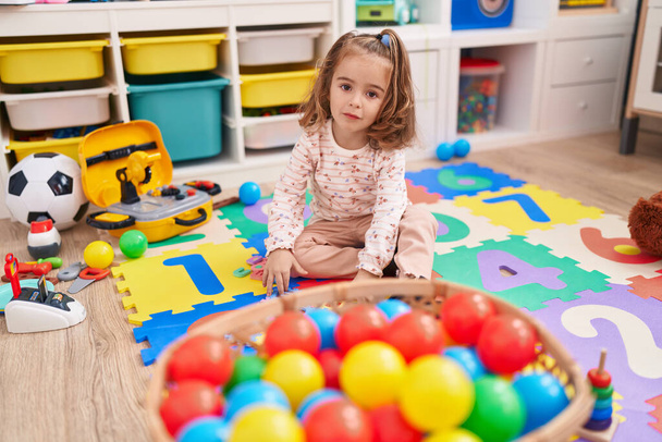 Urocza latynoska dziewczyna bawiąca się piłkami siedząca na podłodze w przedszkolu - Zdjęcie, obraz