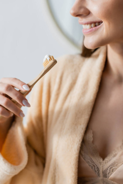 cropped view of smiling woman in bathrobe holding toothbrush with toothpaste in bathroom  - Photo, image