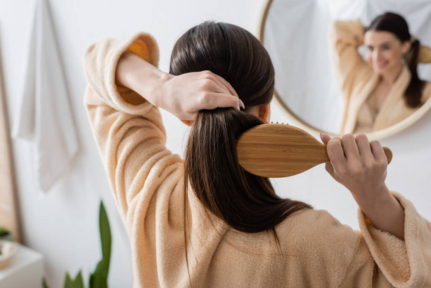 back view of young brunette woman brushing hair in bathroom  - Valokuva, kuva