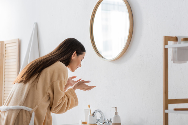 giovane donna bruna con gli occhi chiusi lavaggio viso in bagno  - Foto, immagini