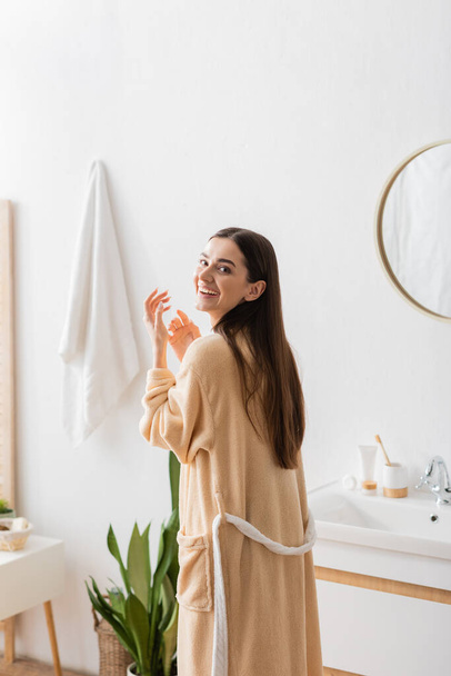 pozitív nő fürdőköpenyben nézi kamera és nevet a fürdőszobában  - Fotó, kép
