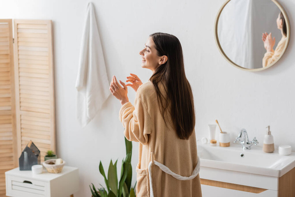 позитивна жінка в халаті сміється біля дзеркала в сучасній ванній
  - Фото, зображення