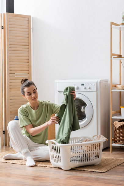 Young woman taking clothes from basket in laundry room  - Foto, afbeelding