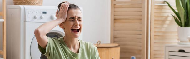 sad woman touching head and crying in laundry room, banner  - Foto, Imagen