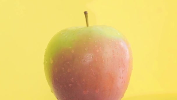 Close-up van appel met waterdruppels geïsoleerd op gele achtergrond in studio. Langzame beweging - Video