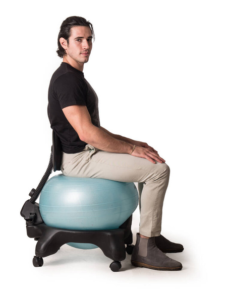 Full body of male sitting on balance ball chair with hands on knees on white background looking at camera - Foto, Bild