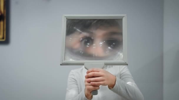 развлечения и наука, веселый мальчик играет с увеличительным стеклом и весело искажает лицо в помещении - Кадры, видео