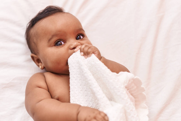 Afrika kökenli Amerikalı bebek yatak odasında battaniye ısırıyor. - Fotoğraf, Görsel