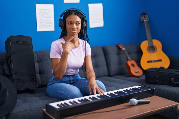Africká Američanka s copánky hrající na klavír klávesnice v hudebním studiu seriózní tvář přemýšlení o otázce s rukou na bradě, přemýšlivý o matoucí nápad  - Fotografie, Obrázek