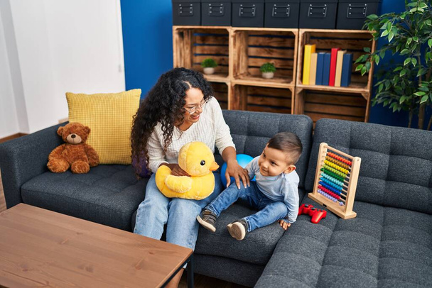Мать и сын играют в игрушки, сидя дома на диване - Фото, изображение