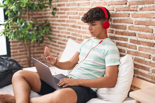 Hispanic teenager using laptop at home sitting on the bedroom with open hand doing stop sign with serious and confident expression, defense gesture  - Fotó, kép