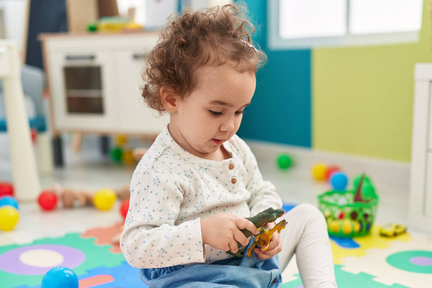 Adorable niño hispano jugando con dino juguete sentado en el suelo en el jardín de infantes - Foto, Imagen