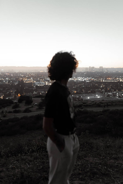 Μια θέα του αστικού τοπίου του Λος Άντζελες με έναν θολό νεαρό άντρα να κοιτάζει κατά τη διάρκεια του ηλιοβασιλέματος στο Μπάλντουιν Χιλς του Λος Άντζελες. Έννοια του τρόπου ζωής - Φωτογραφία, εικόνα