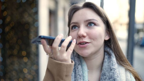 Young blonde woman smiling confident sending voice message by smartphone at street - 写真・画像