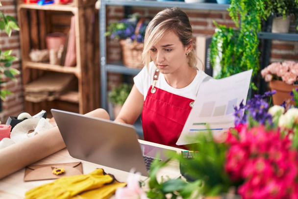 Nuori blondi nainen kukkakauppa käyttäen laptop käsittelyssä asiakirja kukkakauppa - Valokuva, kuva