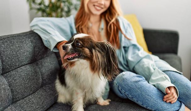 Young caucasian woman smiling confident sitting on sofa with dog at home - Fotoğraf, Görsel