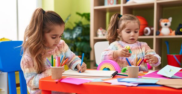 Two kids preschool students sitting on table drawing on paper at kindergarten - Photo, image