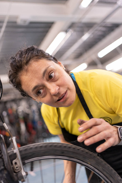 девушка фиксирует велосипед прослушивания сосредоточены на шум колеса, чтобы внести коррективы на велосипеде. Мастерская самообслуживания с девушкой в черном фартуке и желтой футболке. - Фото, изображение