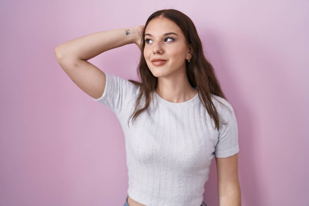 Young hispanic girl standing over pink background smiling confident touching hair with hand up gesture, posing attractive and fashionable  - Fotoğraf, Görsel