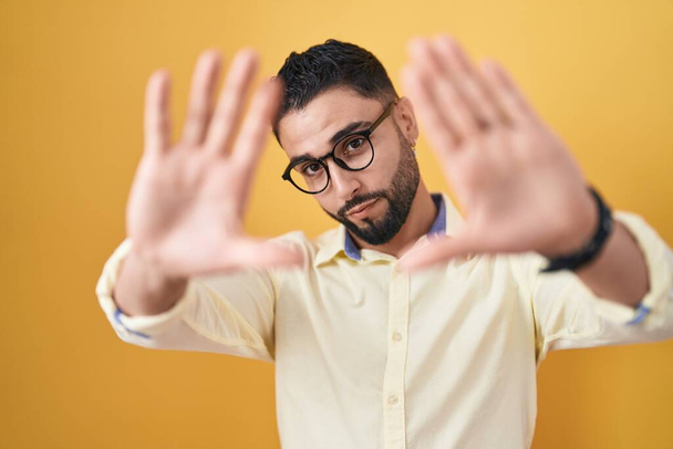 Hispanic young man wearing business clothes and glasses doing frame using hands palms and fingers, camera perspective  - Fotó, kép