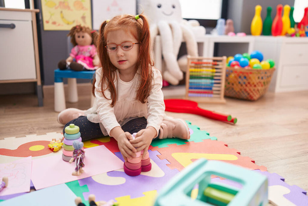 Suloinen punapää tyttö leikkii leluja istuu lattialla päiväkodissa - Valokuva, kuva