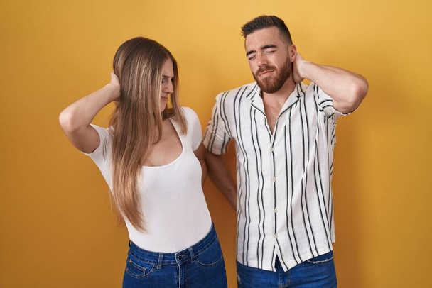 Young couple standing over yellow background suffering of neck ache injury, touching neck with hand, muscular pain  - Foto, immagini