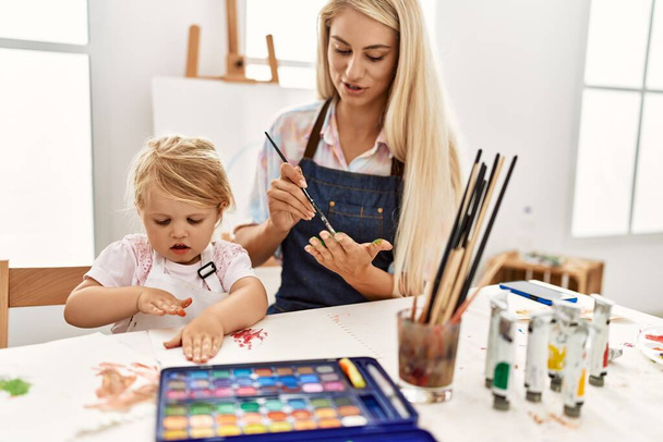 Mother and daughter smiling confident painting palm hands at art studio - Photo, Image